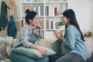 Two women sit closely on couch and discuss mental health treatment programs