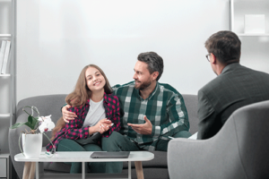 Teen embraces dad as they talk to therapist during family therapy program